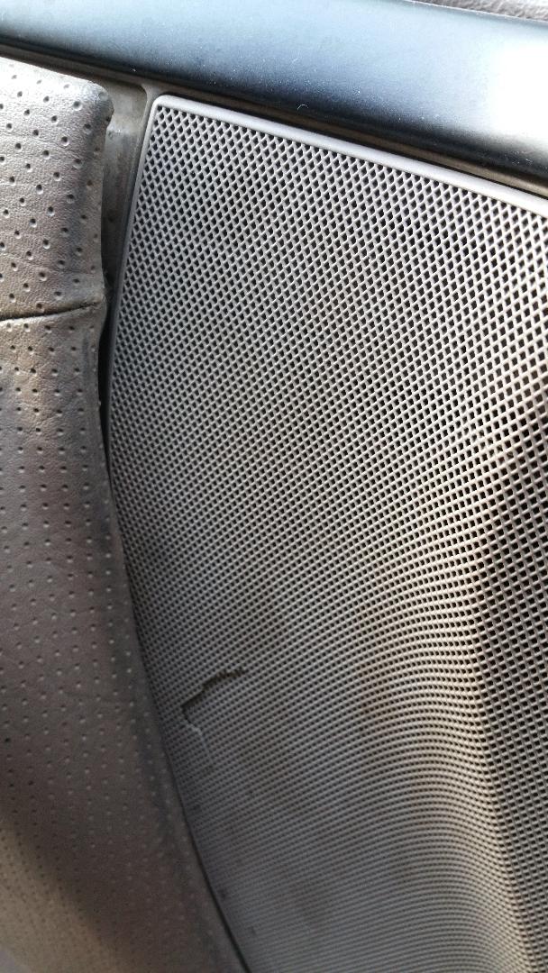 Close-up of perforated leather seat next to a damaged speaker grille inside a vehicle