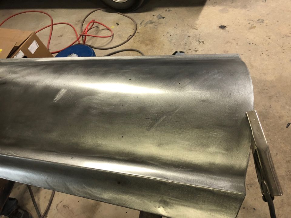 Bare metal car door panel on a workbench with tools and cords in the background