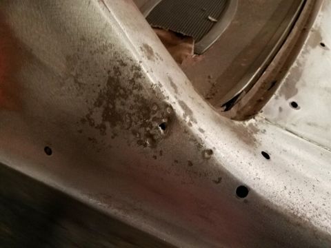 1968 Mercury Cougar - Close-up of a corroded metal car component, possibly a fender or body panel, with visible holes and a hint of a grille in the background.