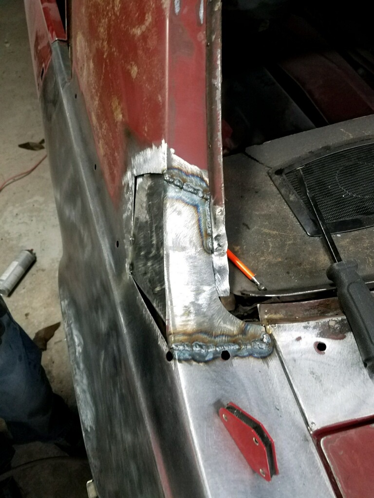 Welding repair on red car's rear quarter panel, showing metalwork