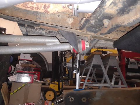 1985 Ford Bronco - Close-up of vehicle undercarriage, focusing on suspension and exhaust parts, with workshop items in the background.