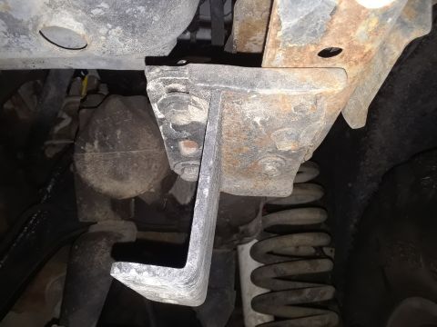 1985 Ford Bronco - Close-up view of a rusted metal bracket and suspension spring under a vehicle.