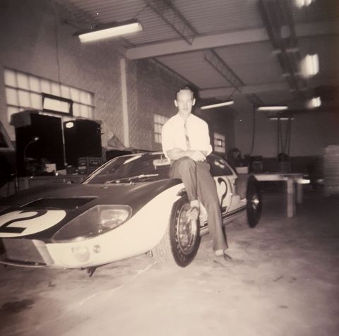 1973 Ford Mustang - A man sits on the hood of a Ford GT40 race car, identified by its distinctive body style and racing number 2.
