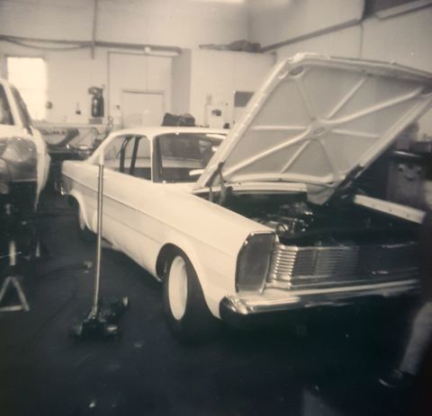 1973 Ford Mustang - White sedan in a garage with its hood open, another vehicle is partially visible to the left.
