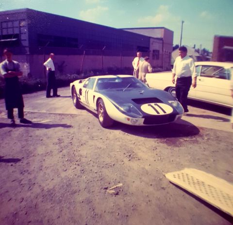 1973 Ford Mustang - A Ford GT40 race car is parked outside a building, with several people observing it.