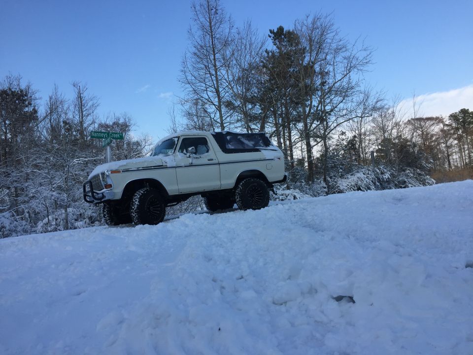 Lifted white 1979 Ford Bronco in snow with "Nanneys Creek" sign.
