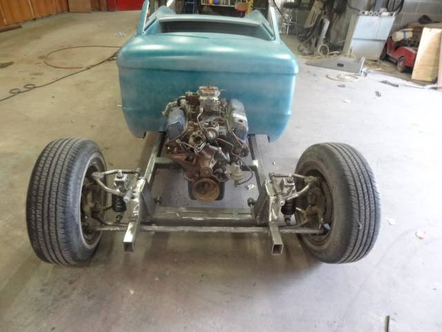 Teal hot rod chassis with V8 engine and front suspension visible in a workshop.