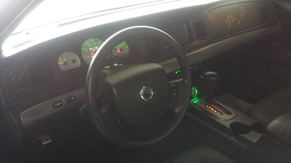 Car interior dashboard with illuminated green gauges, steering wheel, and a signature on the dash.