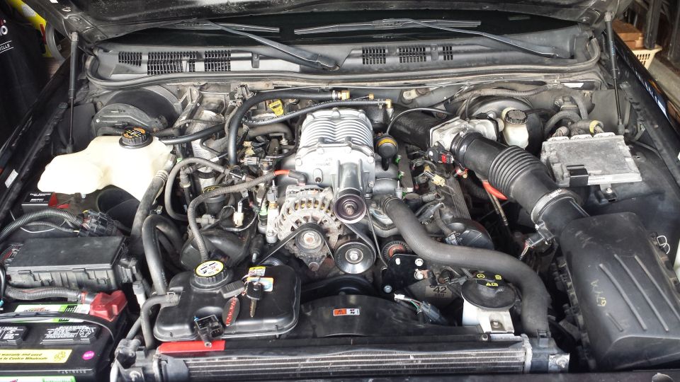 Mercury Grand Marquis engine bay with supercharger, battery, and hoses.