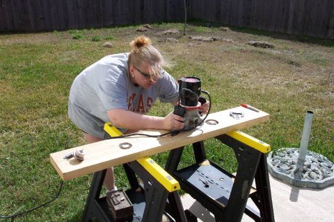 1992 Ford Bronco - A person in a gray Texas t-shirt and safety glasses uses a handheld router on a wide wooden board clamped across yellow-and-black sawbucks…