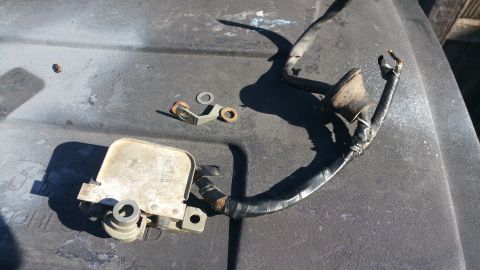 1996 Ford Bronco - A close-up view of a used automotive part with wiring and a metal bracket, resting on a dark, textured surface.