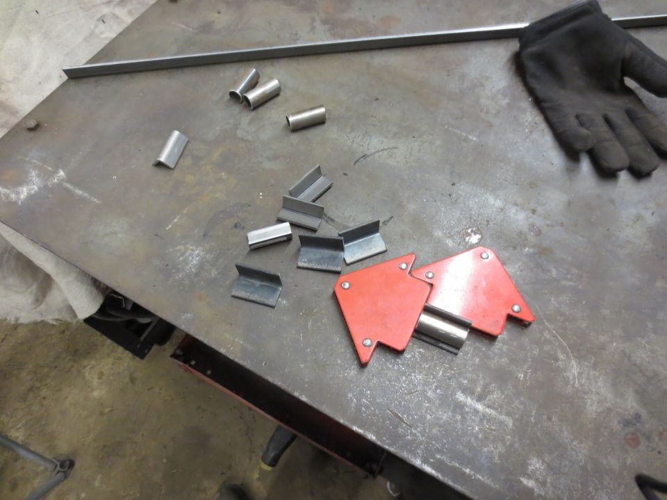 Welding supplies on a workbench including metal pieces, magnets, and a glove.