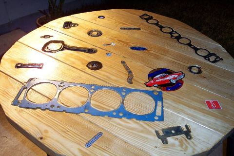 1992 Ford Bronco - Various engine gaskets and car emblems are laid out on a wooden table, including a red classic car emblem.