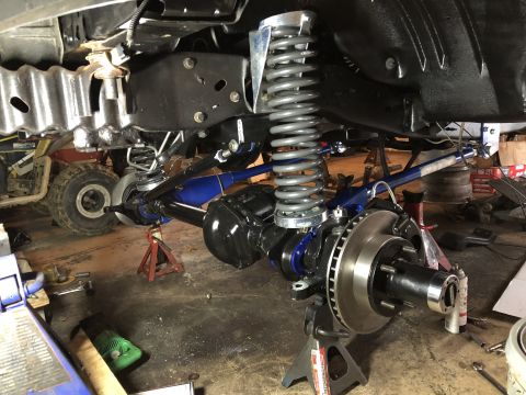 1995 Ford F-150 - The front suspension and axle assembly of a vehicle is shown, supported by jack stands in a garage setting. Visible components include larg…