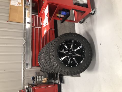 1995 Ford F-150 - A stack of four off-road tires with black and silver rims is leaning against a red toolbox and a silver metal cabinet. The tires appear to…