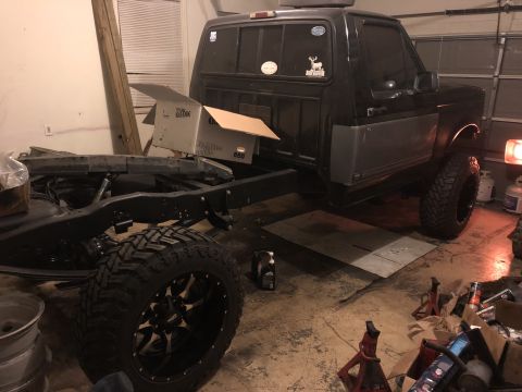 1995 Ford F-150 - A black Ford F-150 pickup truck is parked in a garage with its frame and suspension components visible. The truck has large off-road tires…