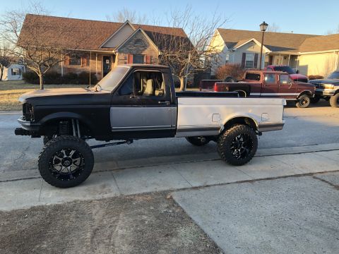 1995 Ford F-150 - A lifted, two-tone pickup truck with black and silver paint is parked on a residential street. The truck has large aftermarket wheels and t…