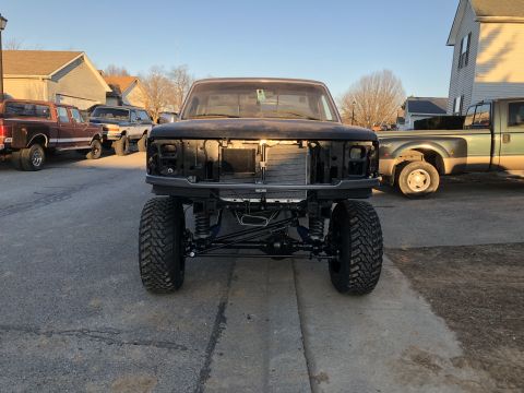 1995 Ford F-150 - A heavily modified black Ford F-Series pickup truck is shown from the front, featuring a lifted suspension and large off-road tires. Other…