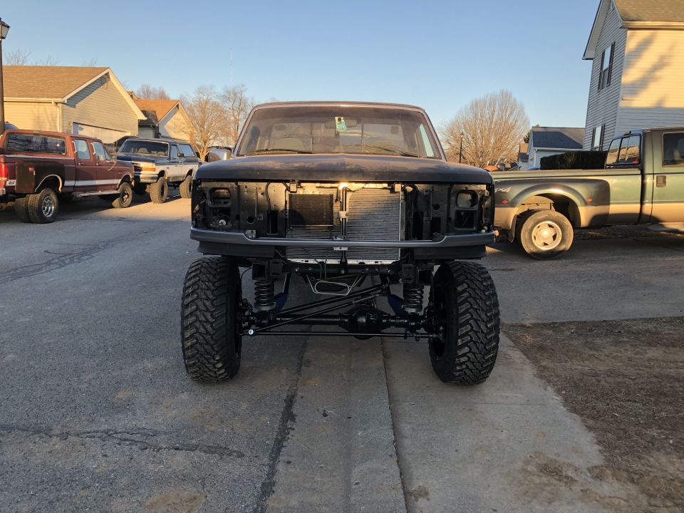 Front view of a lifted black 1990s Ford F-Series pickup truck with custom suspension and large tires.