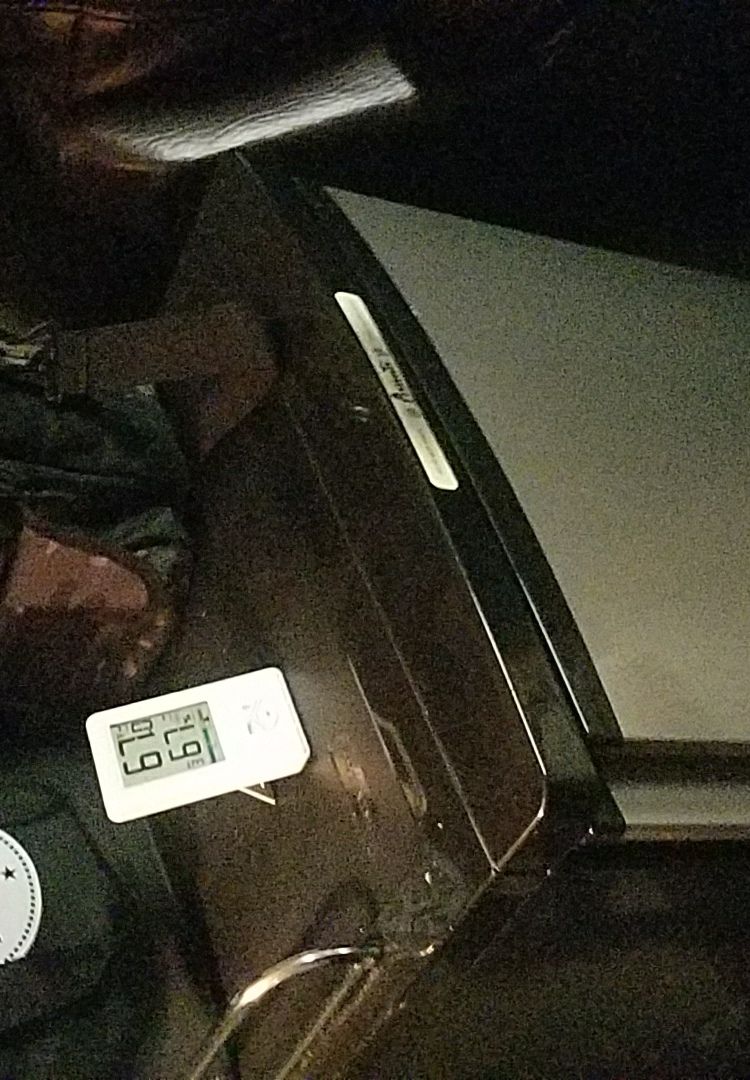 Digital thermometer showing 67.9 degrees on a dark car interior surface with a reflective strip.