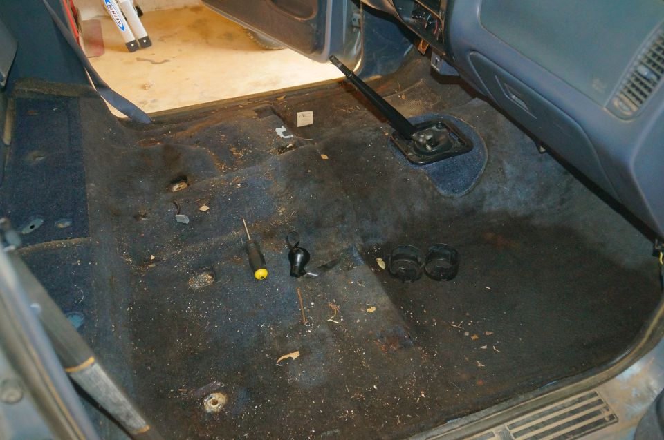 Interior of a dirty vehicle with blue carpet, gear shifter, and tools.