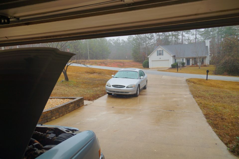 Silver sedan on a wet driveway, with another vehicle's open hood in the foreground.