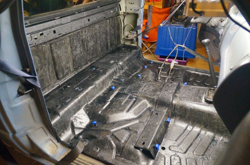 Interior of a pickup truck cab with bare metal floor coated in black protective material and blue clips.