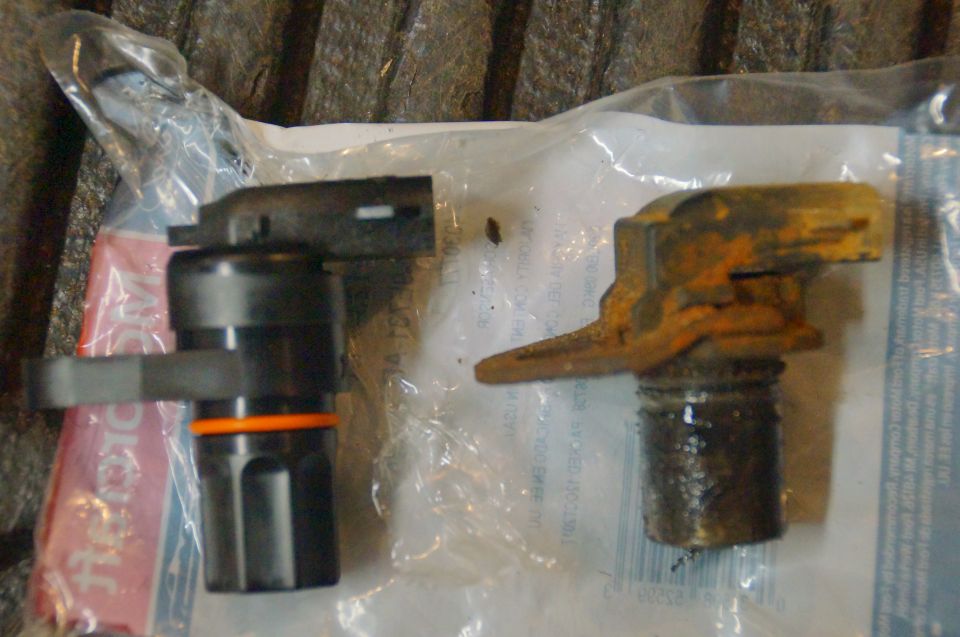New black automotive sensor next to a rusty old sensor in plastic packaging