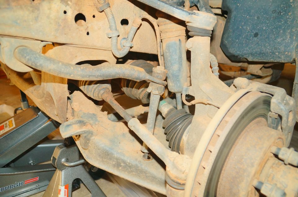 Front suspension and brake assembly of a dirty and rusty vehicle, likely a Ford Ranger.