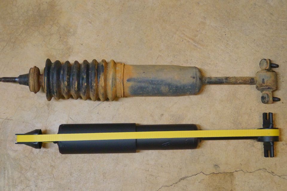 Two shock absorbers, one old and rusty, one new and black with a yellow measuring tape.