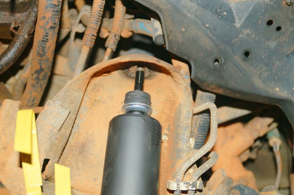 Top of a black shock absorber with threaded shaft and washer on rusty vehicle suspension.