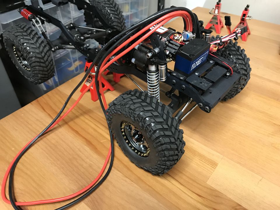 RC rock crawler chassis with tires, motor, ESC, and wiring.