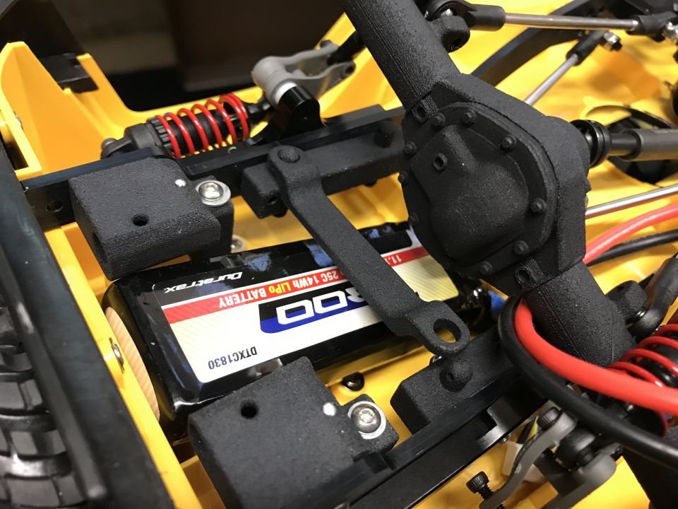Close up of RC car parts: yellow chassis, black differential, red shock, Duratrax battery.
