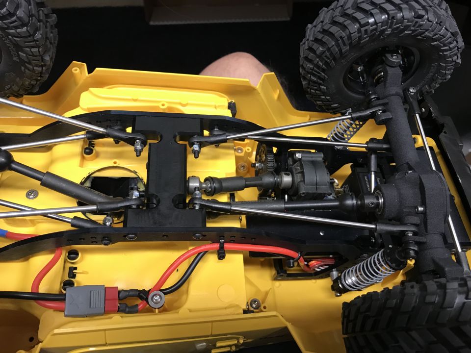 Underside of yellow RC car chassis with suspension, drivetrain, and wiring.