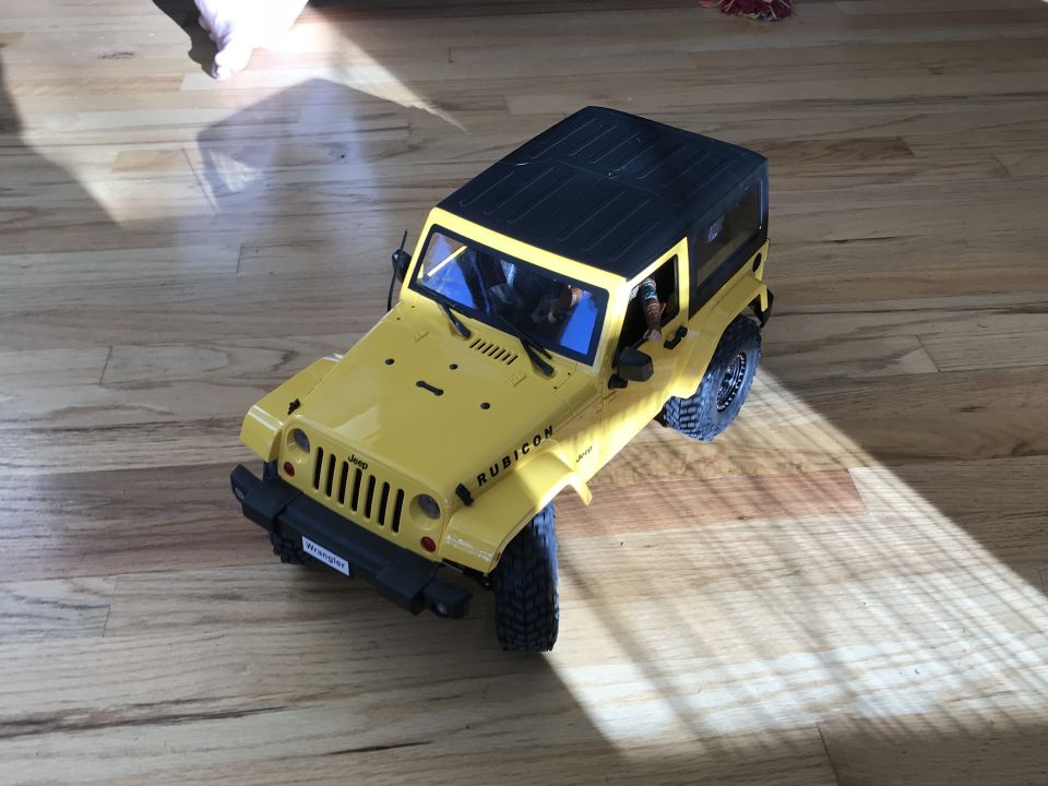 Yellow RC Jeep Wrangler Rubicon on a wooden floor with sunlight and shadows.