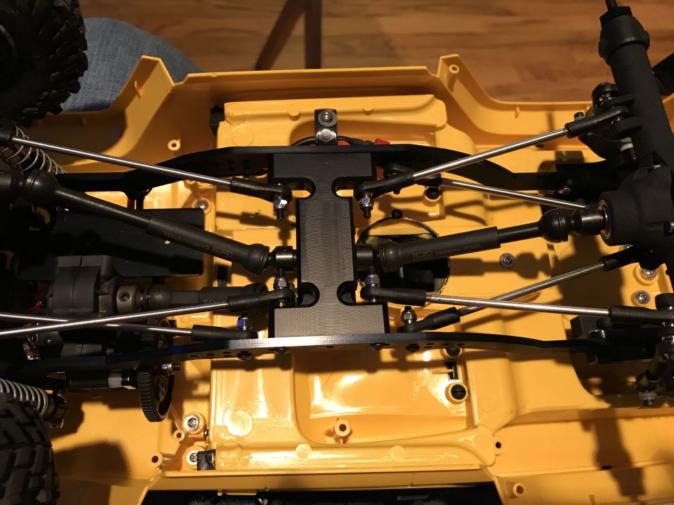 Underside of a yellow RC car chassis with black metal suspension parts and linkages.