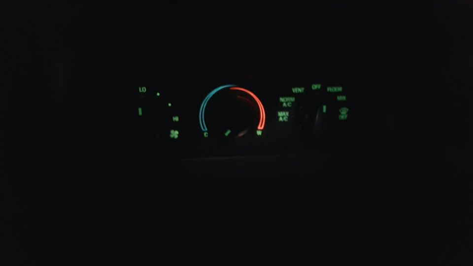 Car climate control panel at night with temperature, fan speed, and air direction settings.