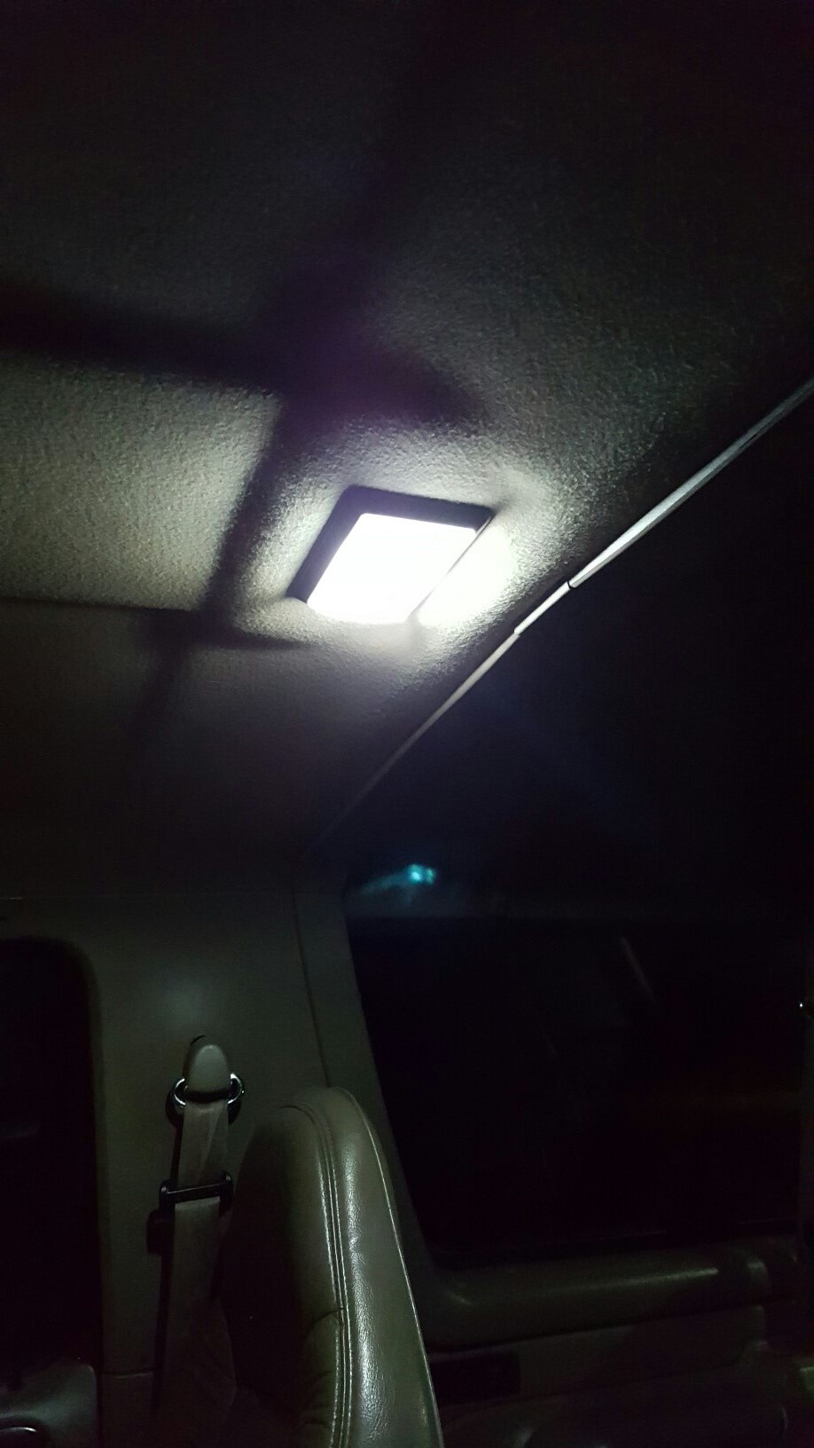 Interior of an SUV showing a lit dome light and tan seatbelt.