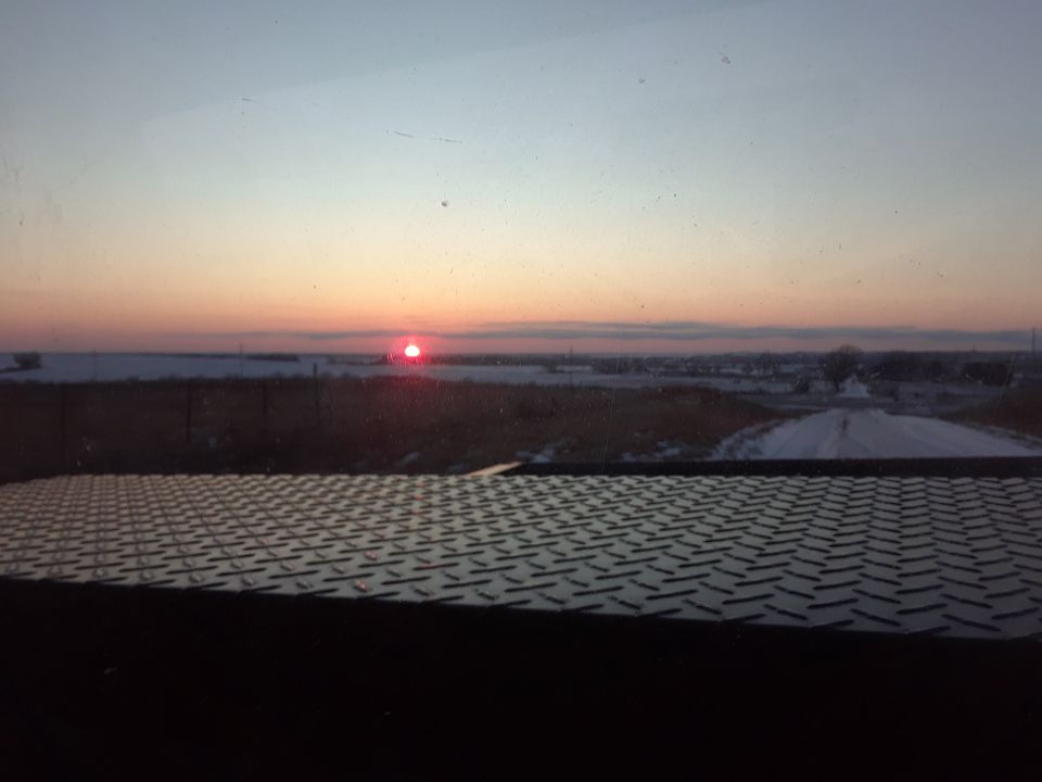 Sunset over a snowy landscape with a textured metal surface in the foreground.