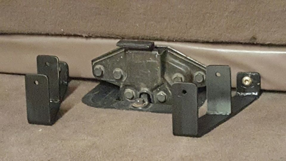 Black metal latch mechanism with brackets on brown carpet.