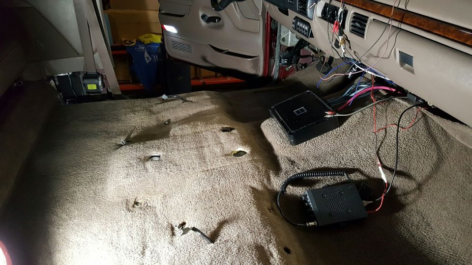 Interior of a vehicle with carpet removed, showing wiring, amplifier, and CB radio on the floor.