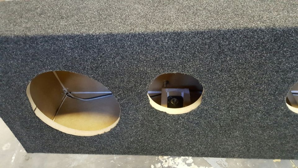 Gray carpeted speaker box with three circular cutouts, two visible