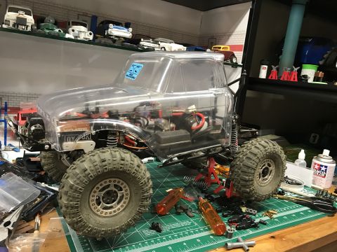 1989 Ford Bronco - A clear-bodied RC rock crawler truck sits on a workbench, surrounded by tools and parts, ready for assembly or modification.