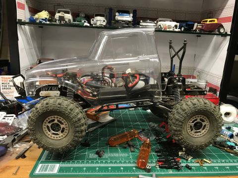 1989 Ford Bronco - An RC truck chassis with a clear body sits on a green cutting mat surrounded by tools and parts.