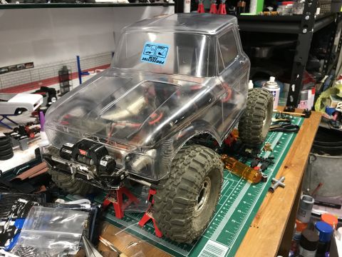 1989 Ford Bronco - RC truck body on jack stands, with tools and parts scattered around a workbench.