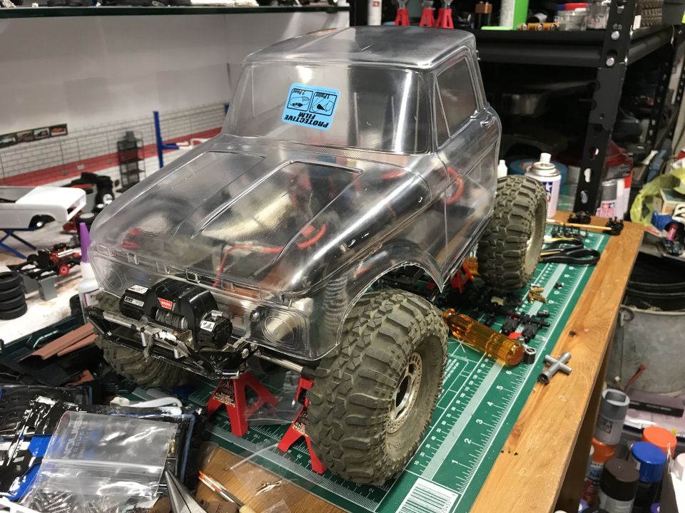 Clear plastic RC truck body with winch mounted on front, resting on red jack stands