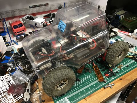 1989 Ford Bronco - A partially assembled RC crawler truck sits on a workbench surrounded by tools and parts.