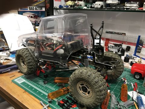 1989 Ford Bronco - An RC truck chassis with a clear body and large tires is assembled on a workbench with various tools.