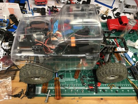 1989 Ford Bronco - RC car chassis with clear body, parts, and tools on a workbench.