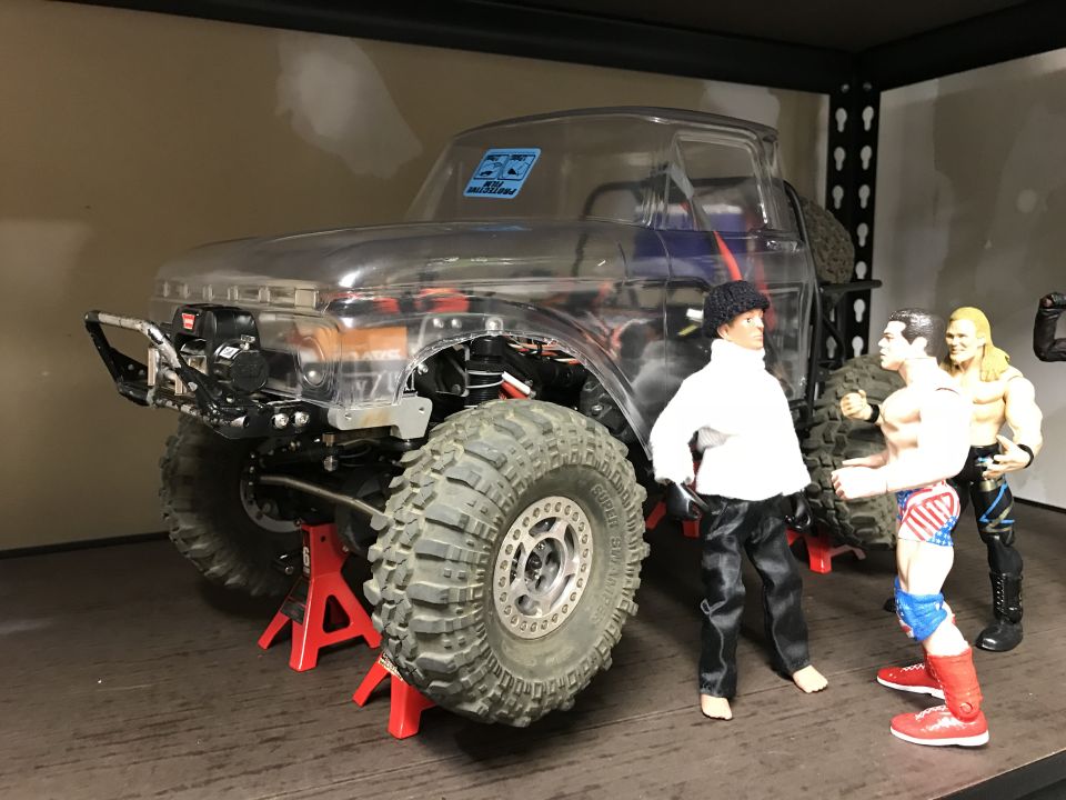 Toy truck with clear body, large tires, and aftermarket bumper, raised on red jack stands